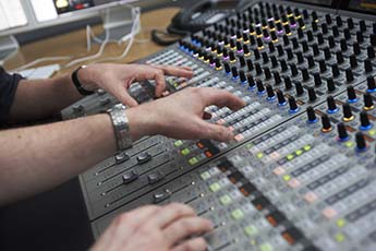 Photo by John Houlihan of two technicians' hands on a music mixing desk.